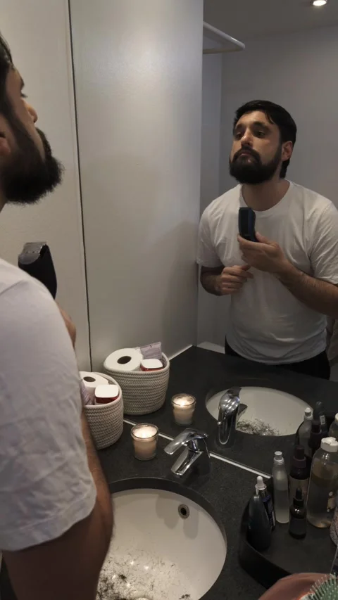 Focused bearded man shaving with electric trimmer in modern bathroom Video stock 335636982