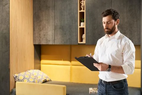 Focused bearded manager looking at tablet, making notes, while standing in Stock Photos