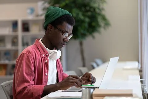Focused black hipster guy remote online works on laptop typing on keyboard in Stock-Fotos