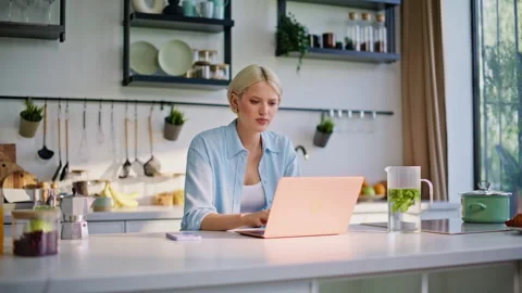 Focused blonde working laptop sitting kitchen table closeup. Woman sipping tea Stock Footage 335150735