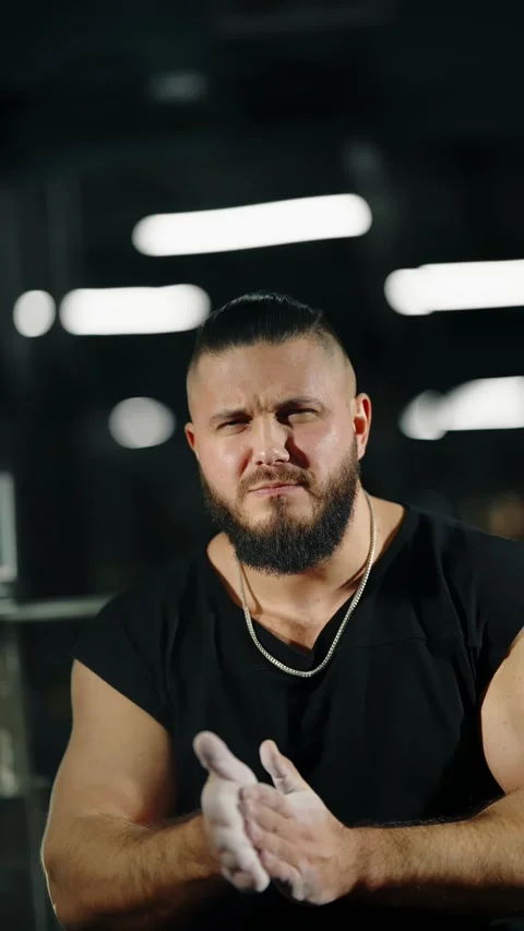 Focused bodybuilder prepares with chalked hands in a dimly lit gym, highlighting 库存影片 329555615