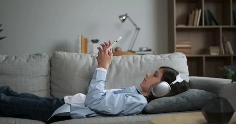 Focused Boy Lying on Couch with Phone and Headphones Stock Footage 254437364