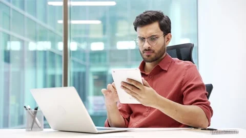 Focused businessman in glasses is using digital tablet while sitting at the desk Stock Footage 288885634