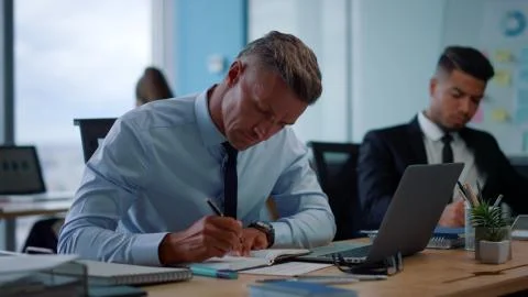 Focused businessman making notes in notebook. Male entrepreneur typing on laptop Stock Photos