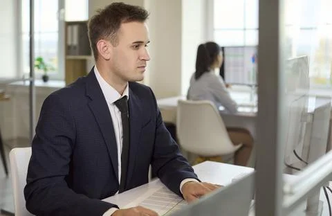 Focused businessman working at computer in office, coworker in background Stock Photos