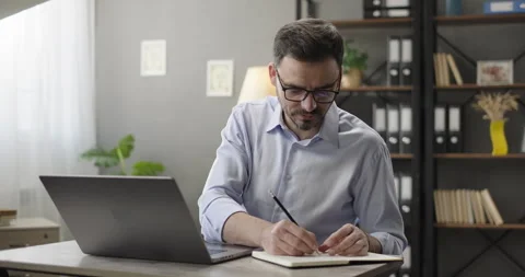 Focused businessman working on laptop computer, making notes at home office Stock Footage 266935527