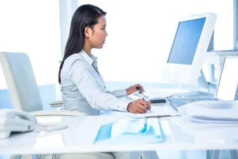 Focused businesswoman taking notes while working on computer 스톡 사진