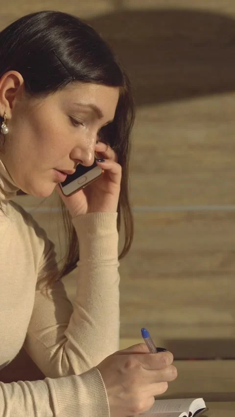 Focused businesswoman writing in a notebook while having a phone conversation Stock Footage 345459807