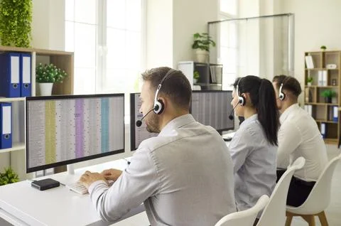 Focused call center operators using headsets at monitors in modern office Stock Photos