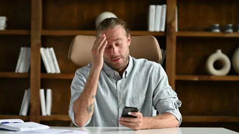 Focused caucasian guy is sitting at a table in a modern office, using his Vídeos de archivo 168384831