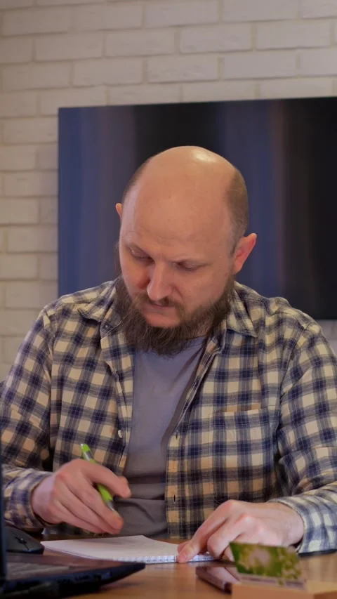 Focused caucasian man completing work at laptop, typing and writing in notebook Stock Footage 344743786