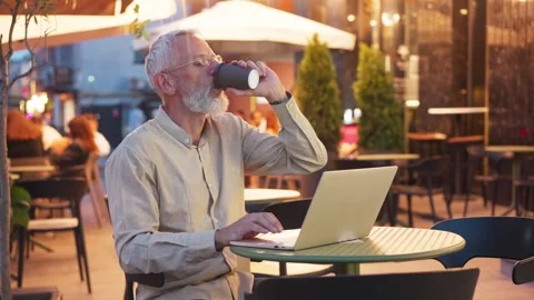 Focused Caucasian man with gray beard and glasses working on laptop at outdoor Stock Footage 311571924