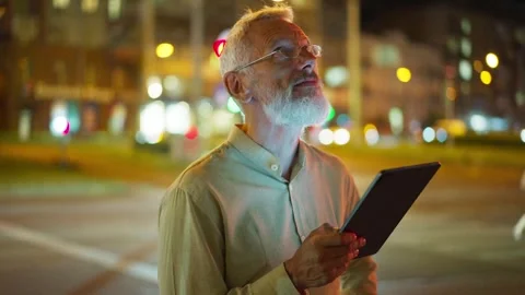 Focused Caucasian man with white beard and glasses holding tablet on city street Stock Footage 311572340