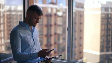 Focused Caucasian young man with document folder surfing Internet on smartphone Stock Footage 213611497