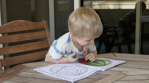 Focused child sits at the table and begins to draw with crayons. Draw moment Video stock 317988603