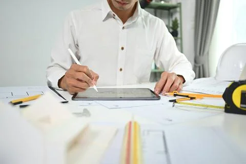 Focused civil engineer man using digital tablet, inspecting construction plan at 写真素材