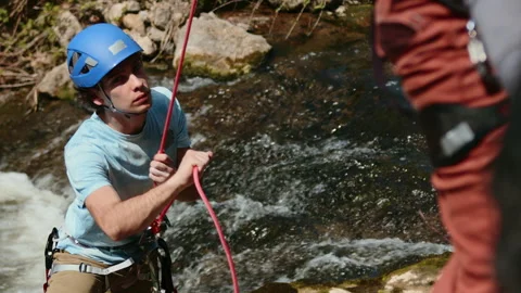 Focused Climber Securing Rope by River, ProRes Capture of Climbing Teamwork in Stock Footage 272818496