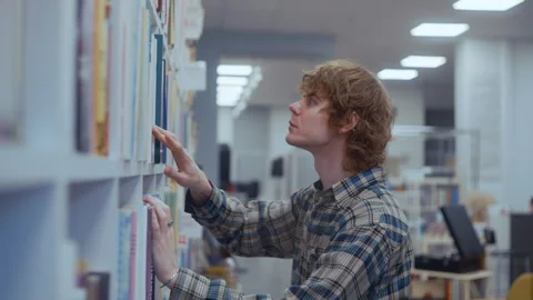 Focused College Guy Browsing Bookshelves for a Study Volume Vídeo Stock 335124256