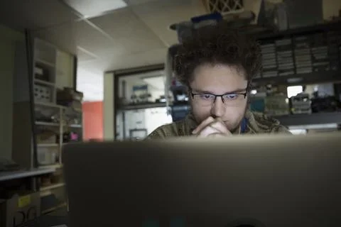 Focused computer programmer working at laptop in dark workshop 写真素材