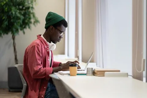 Focused concentrated black freelancer hipster guy sits at desk typing laptop Stock Photos