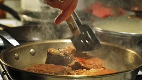 Focused cooking tutorial: frying meat in a metallic pan on a kitchen stove with Stock Footage 338167773