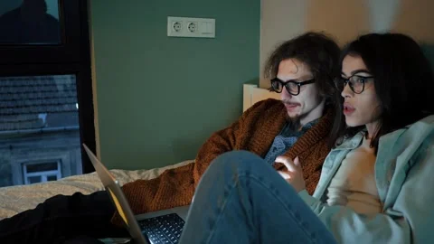 Focused couple on bed engaged with laptop, immersed in screen content together Stock Footage 272926427