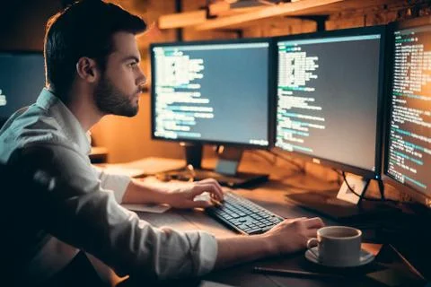Focused developer coding on computer monitors working late in office Stock Photos