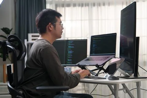 Focused Developer Engaged in Programming Tasks with Multiple Screens Displayi Stock Photos