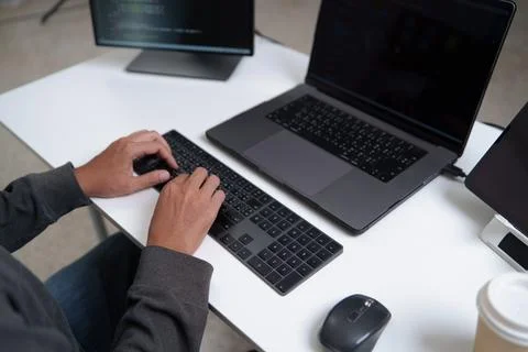Focused Developer Programming Code on Laptop with Multiple Monitors for Sof.. Foto stock