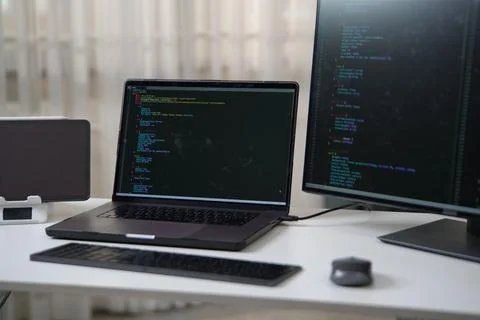 Focused Developer Working on Coding Project with Dual Monitors and Laptop Set Foto stock