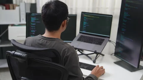 Focused Developer Working on Multiple Screens in a Workspace Environment Stock Footage 336680309