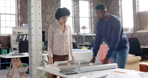 Focused diverse colleagues discussing work at table with building model in Stock Footage 342017935