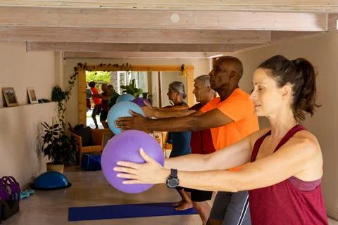 Focused diverse seniors using exercise balls in pilates class with female coach Stock Photos