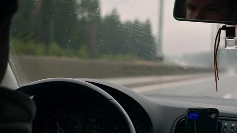 Focused driver on rainy road, steering wheel and water drops on windshield Stock Footage 309677402