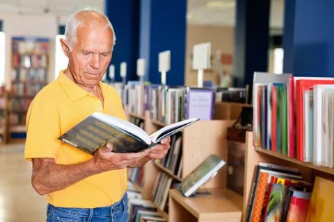 Focused elderly man looking for information in books in bookstore Photos