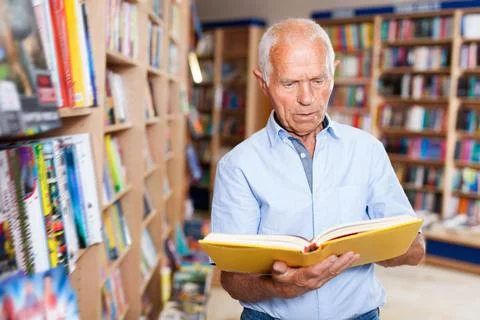 Focused elderly man looking for information in books in bookstore 스톡 사진