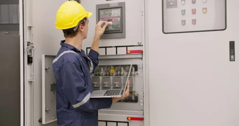 Focused engineer in a hard hat inspects an industrial electrical panel using a l Stock Footage 328595927