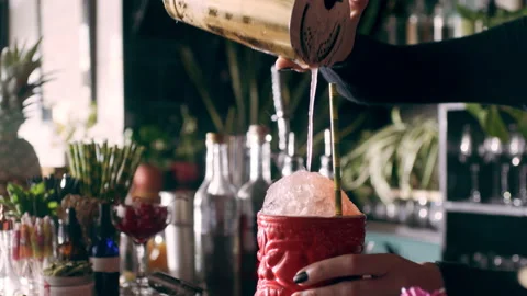 Focused female bartender using a strainer pours the drink in a tiki glass filled Stock Footage 199455593