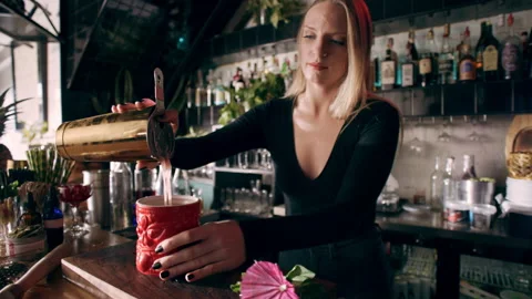Focused female bartender using a strainer pours the drink in a tiki glass and fi Stock Footage 199457441
