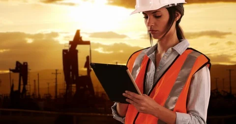 Focused female engineer hard at work on pad device in oilfield by pumpjacks Vidéo 87615004