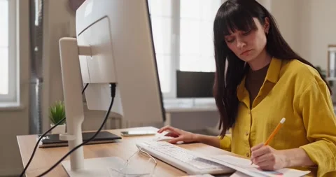Focused female freelancer doing paperwork at computer in bright modern home Stock Footage 335096700