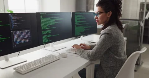 Focused female programmer coding at triple monitor workstation in bright office 動画素材 332765357