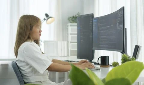 Focused female software developer working with program code on wide display.. Stock Photos