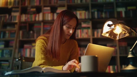 Focused female student doing academic research on laptop in university library Stock Footage 340267182
