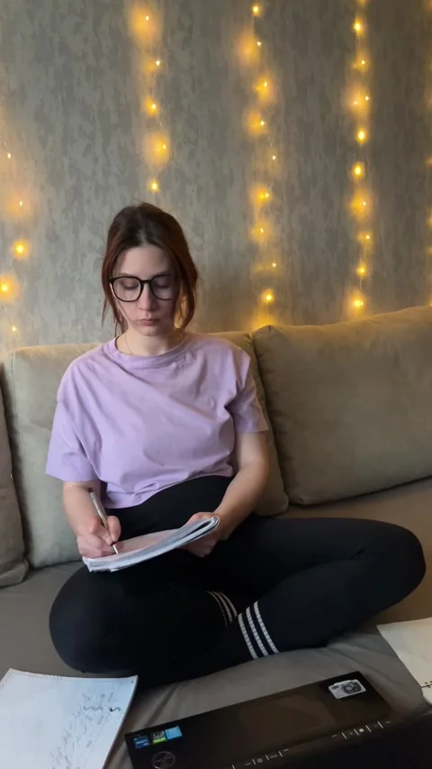 Focused Female Student with Glasses Typing and Writing Notes on Couch Stock Footage 329319600