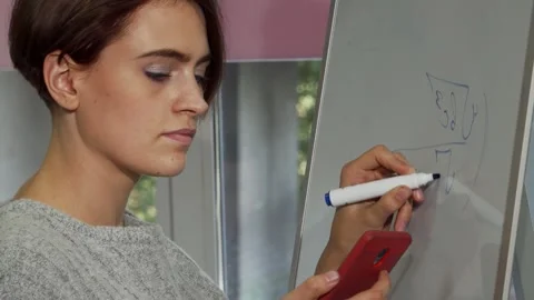 Focused female student solving math problems on her smartphone while writing on Stock Footage 311522469