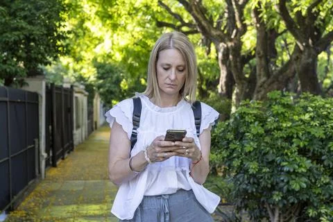 Focused female using her mobile phone to type a message during a quiet walk.. Stock Photos