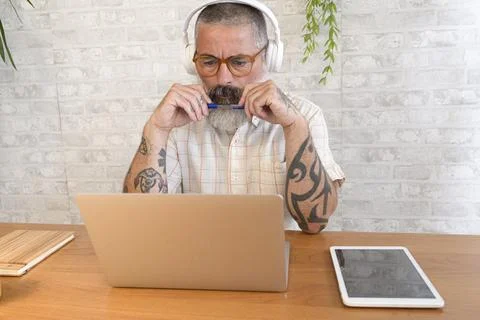 Focused freelancer biting pen while working remotely from home office Stock Photos