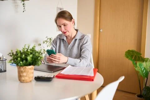 Focused freelancer using smartphone at home office desk 스톡 사진