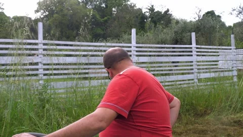 Focused gardener on red tractor mower during lawn maintenance Video stock 307834601